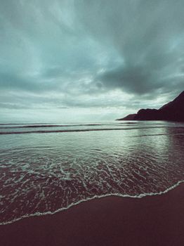 A scenic coastal view with gentle waves and moody overcast skies creating a serene atmosphere.