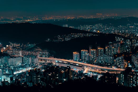 Aerial view of a vibrant cityscape with illuminated buildings and a winding highway at night.