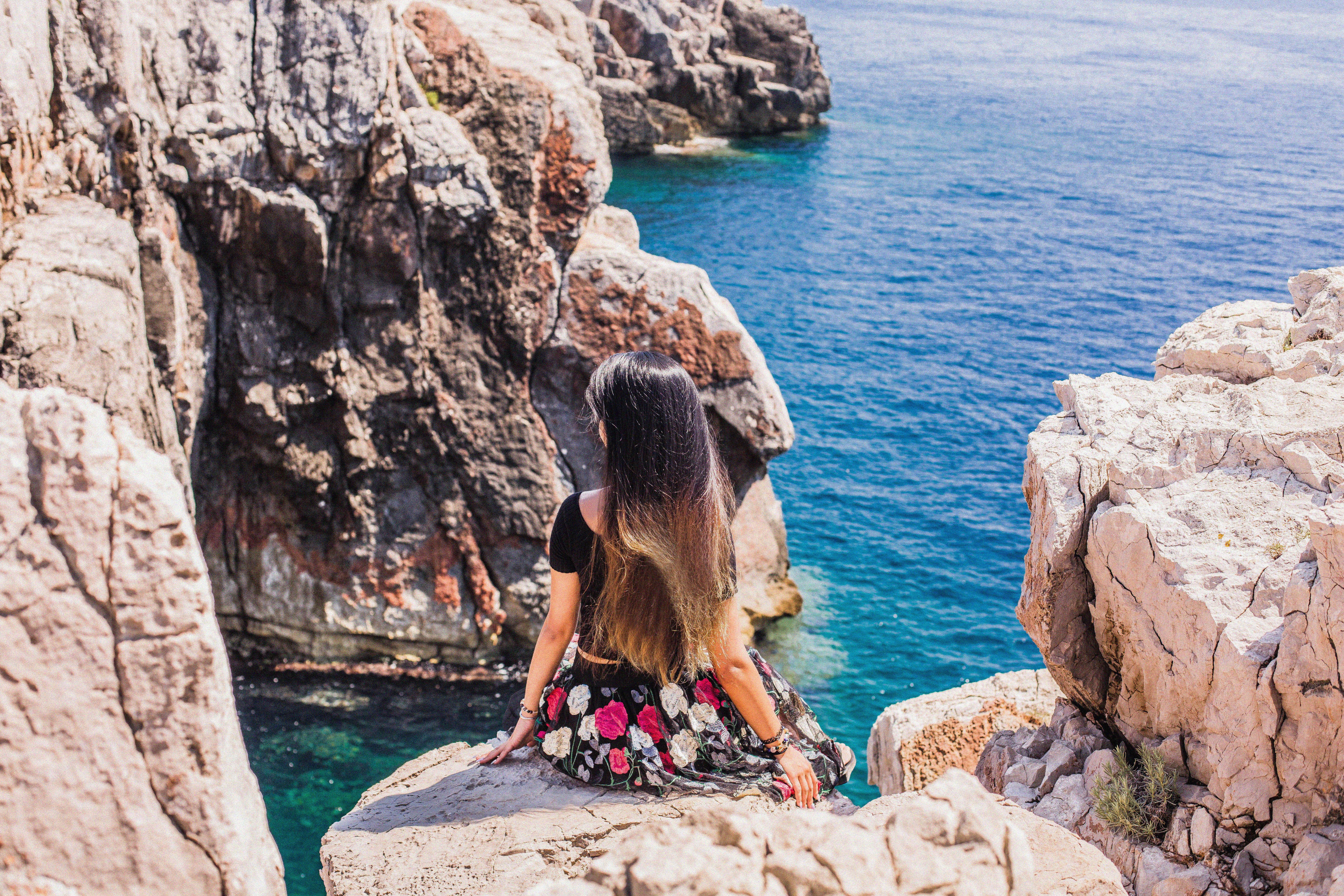 A woman sits on a rocky cliff, gazing at the clear blue Adriatic Sea in Croatia. - Photo by Mavluda Tashbaeva on Pexels