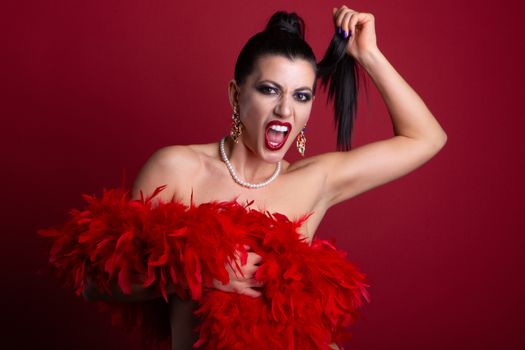 Striking fashion portrait of a woman with red boa and vibrant makeup, set against a red background.
