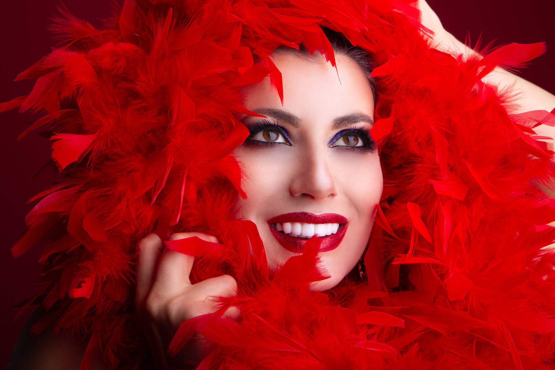 Elegant woman with vibrant red feather boa and captivating smile.