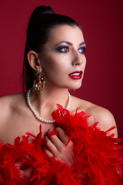 Free A striking portrait of a woman in red feathers and pearls with dramatic makeup. Stock Photo
