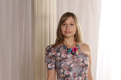 Woman Wearing Grey and Multicolored Floral Single-shoulder Top Against Beige Curtains