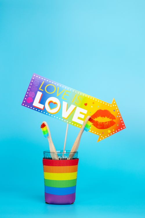 Free Rainbow themed still life image featuring a 'Love is Love' sign and rainbow toothbrushes. Stock Photo