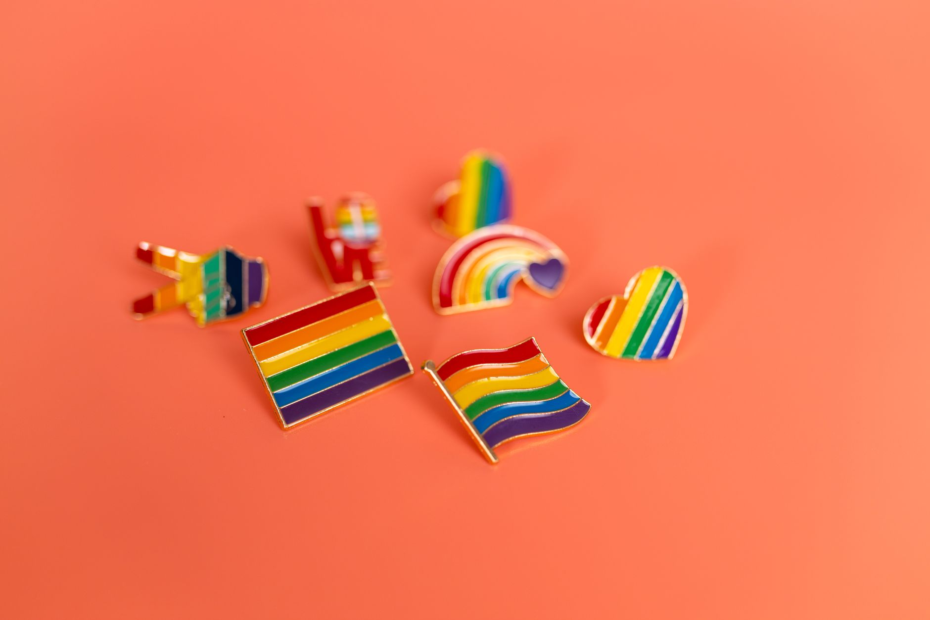Imagen de archivo: Una colección vibrante de insignias del orgullo LGBT con banderas y símbolos del arcoíris sobre un fondo naranja.