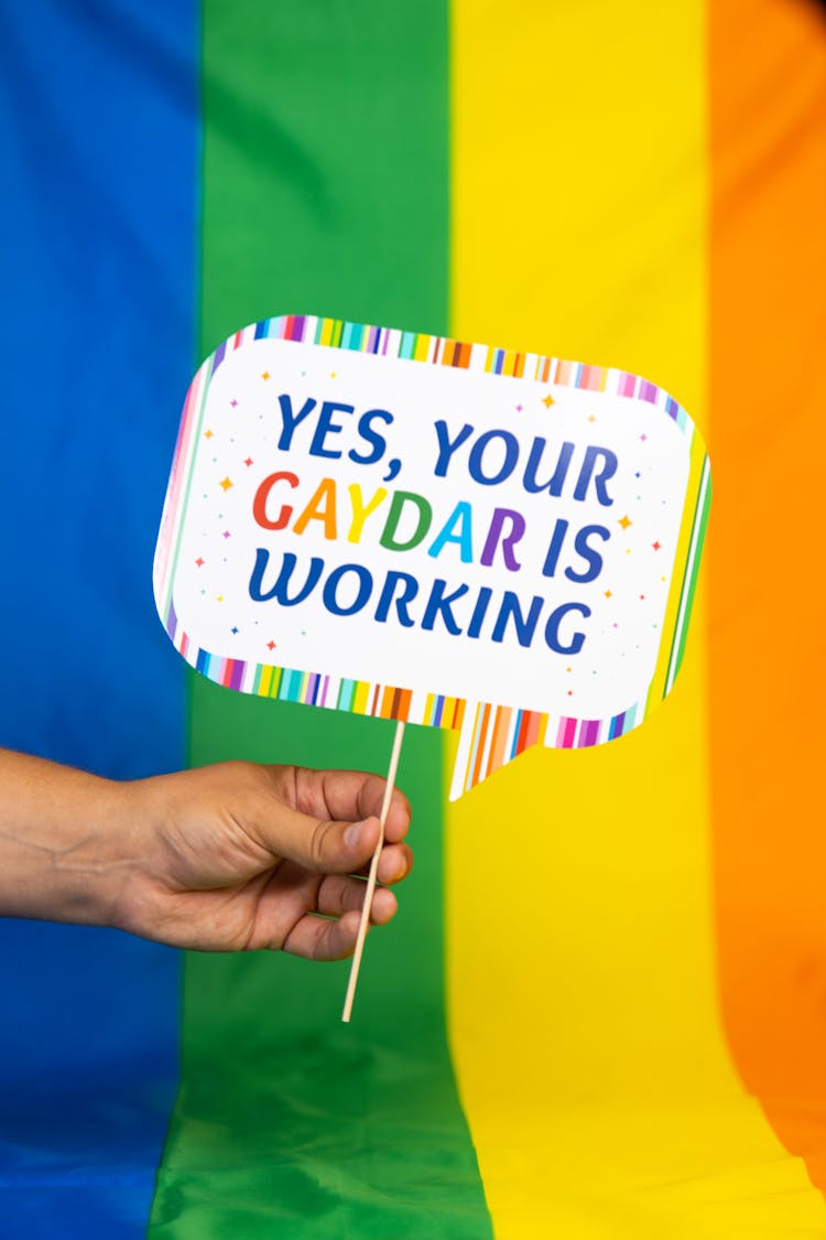 Hand Holding Sign In Front Of Rainbow Flag