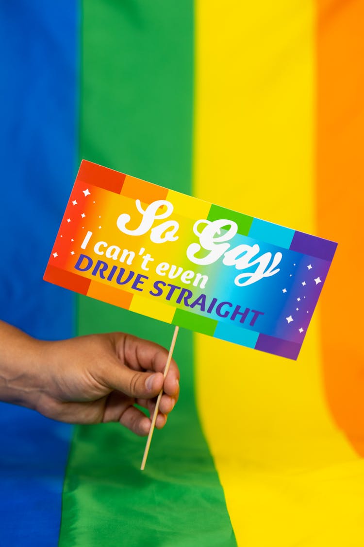 Hand Holding Sign In Front Of Rainbow Flag