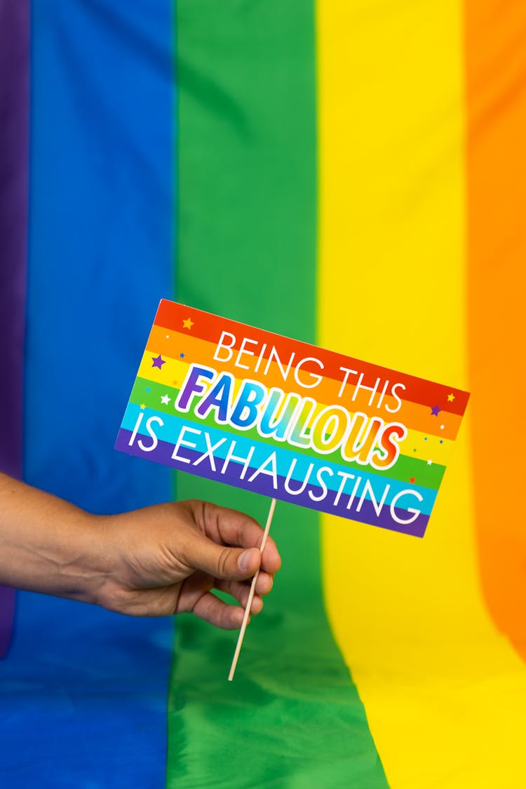 Hand Holding Sign In Front Of Rainbow Flag