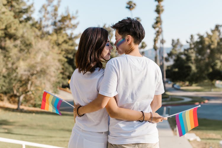 Lesbian Couple Holding Rainbow Flags Embracing 