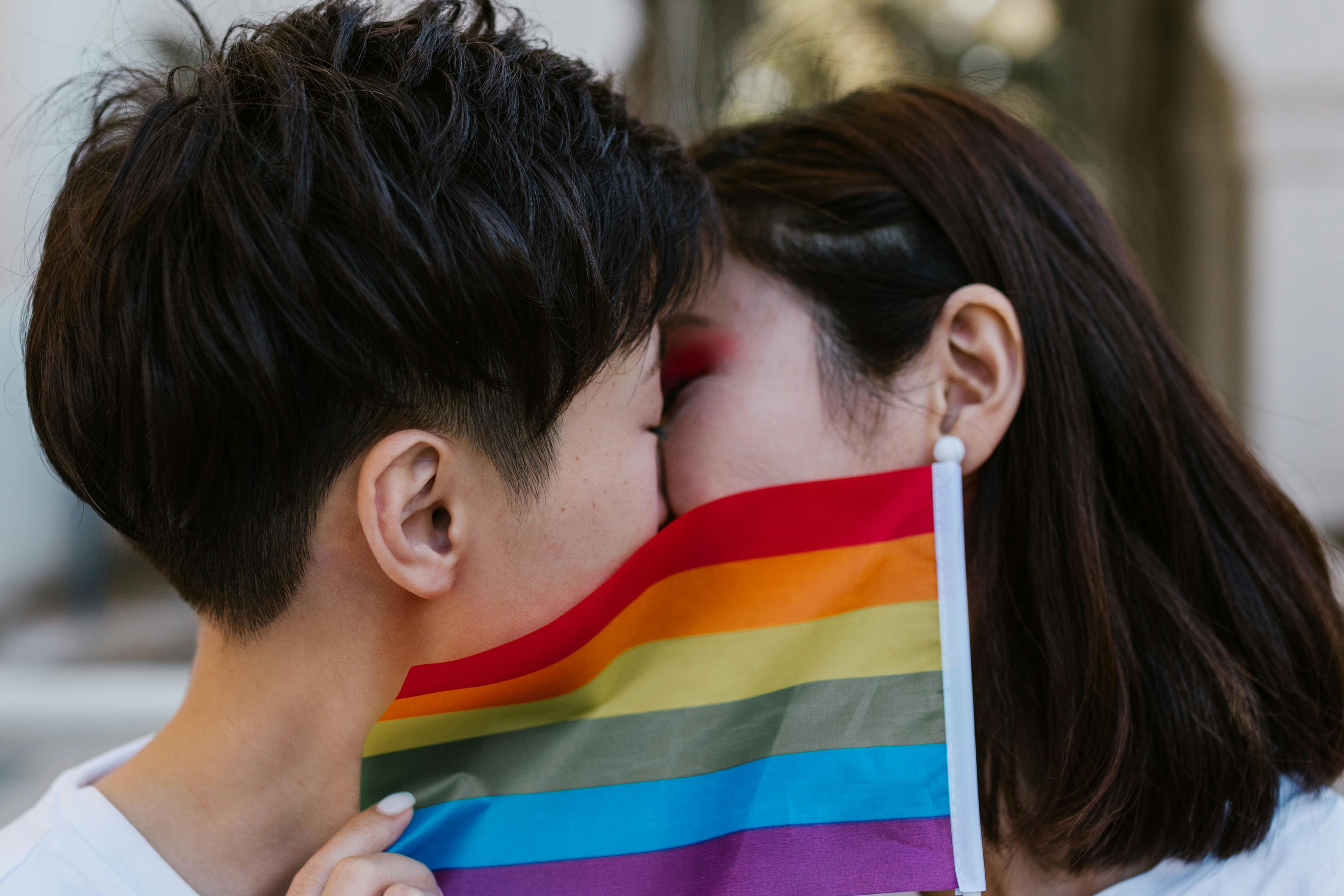 Lesbian Couple Kissing behind Pride Flag · Free Stock Photo