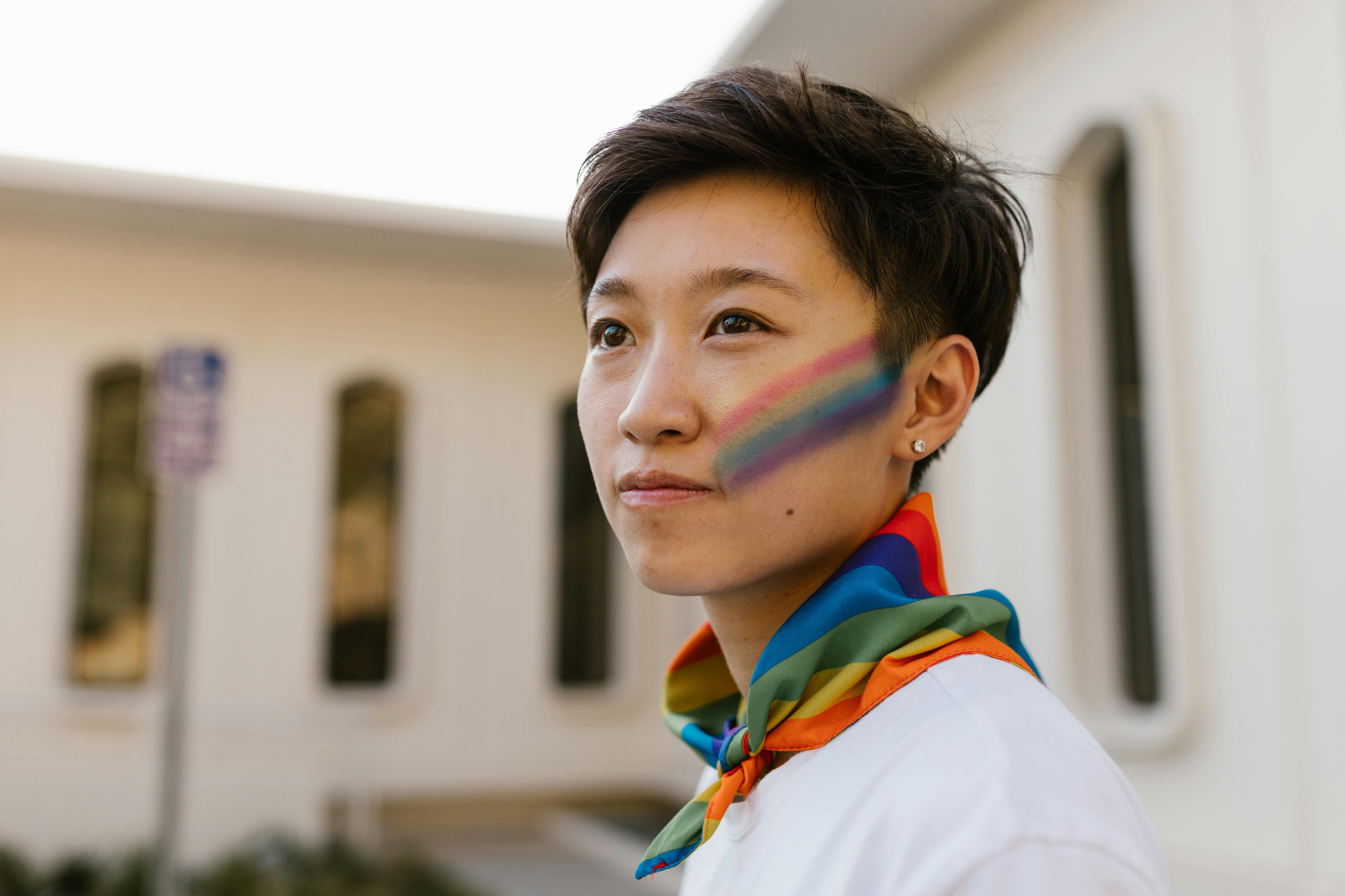 portrait of woman with rainbow face paint and rainbow flag tied around neck