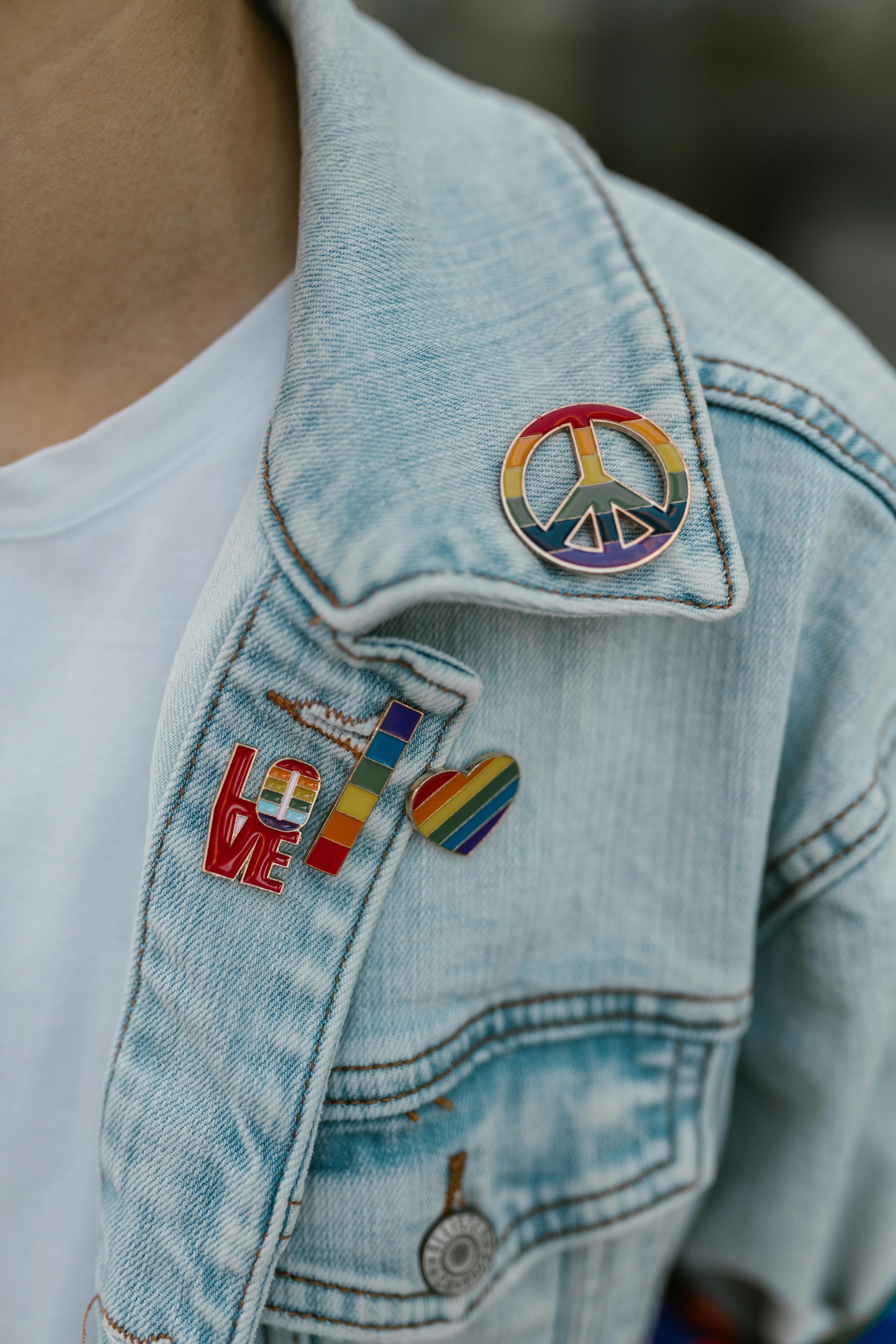 Close-up of a denim jacket adorned with colorful rainbow pride pins, promoting equality.
