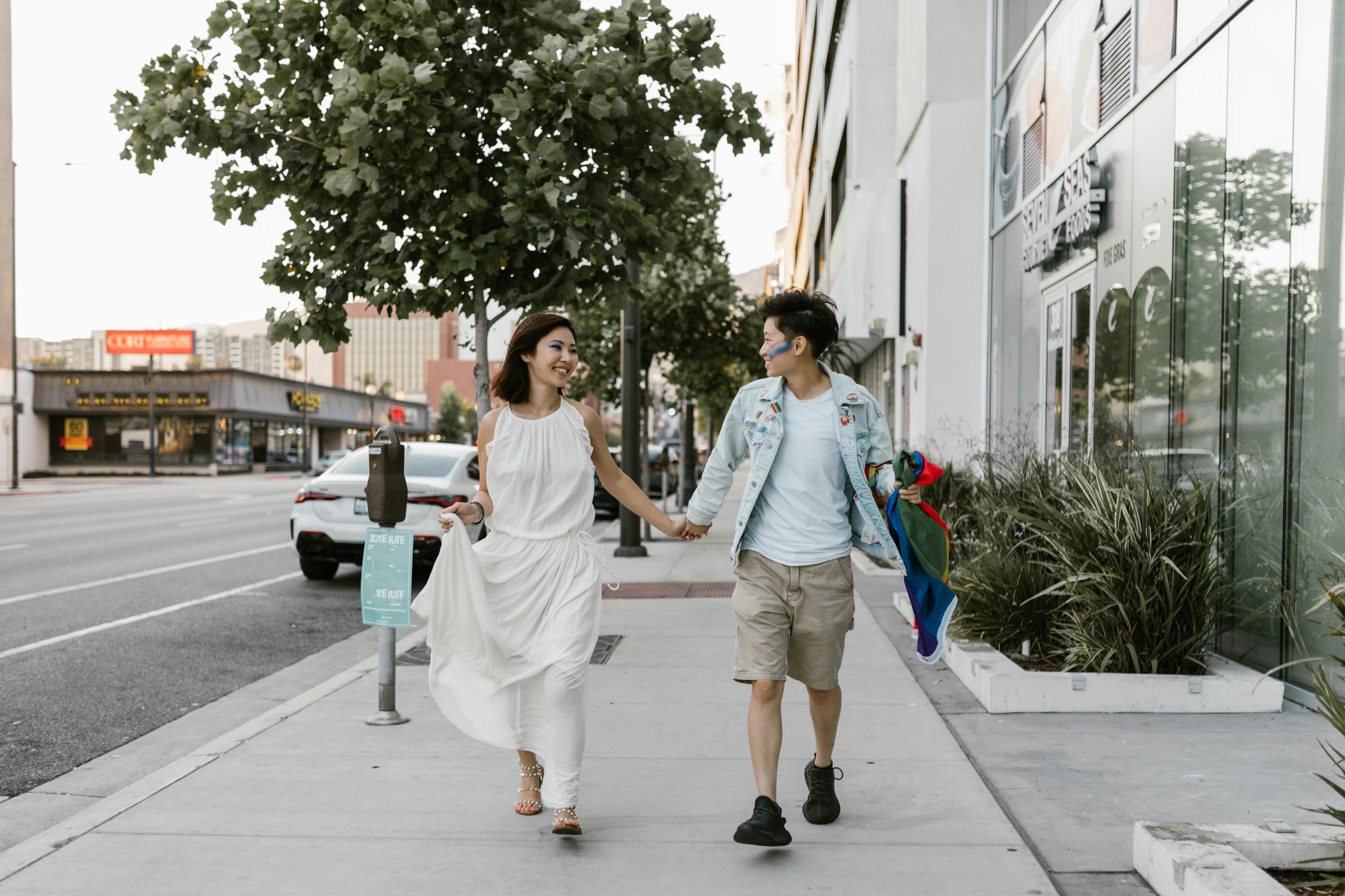 A joyful couple expressing love with a rainbow flag in an urban setting.