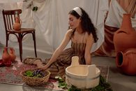 Woman Sitting on a Carpet and Touching a Basket full of Grapes