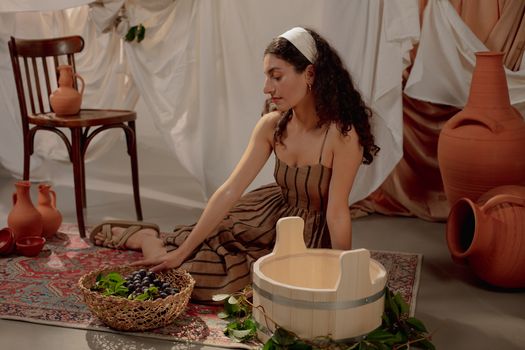 Woman Sitting on a Carpet and Touching a Basket full of Grapes