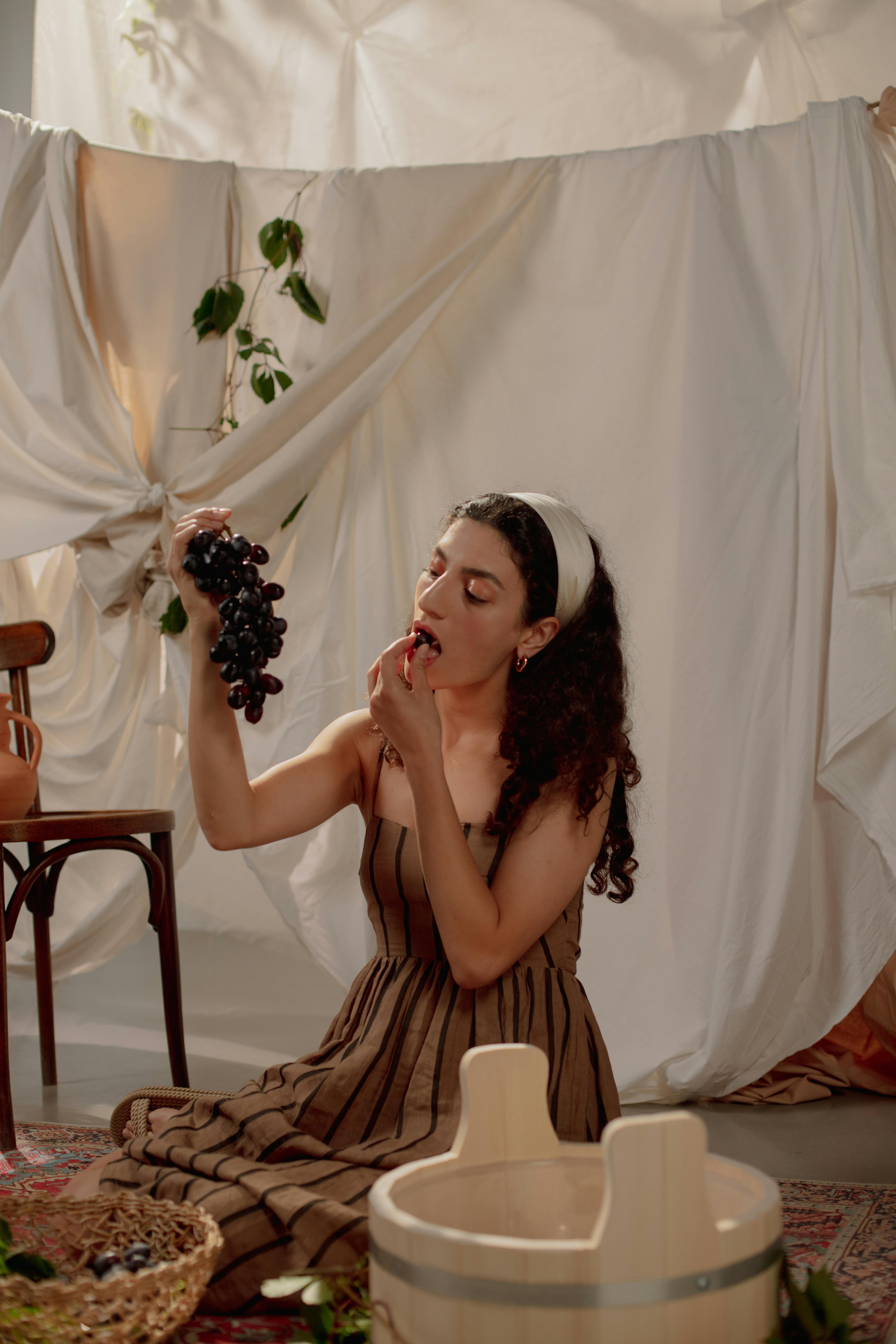 Young woman in striped dress eating grapes, vintage indoor scene