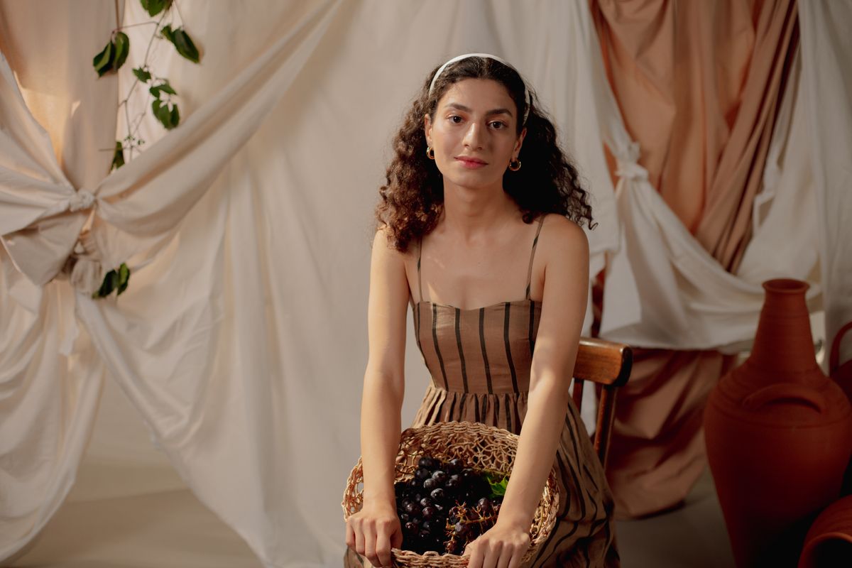 Mujer con vestuario inspirado en la antigua Roma sosteniendo una cesta de uvas