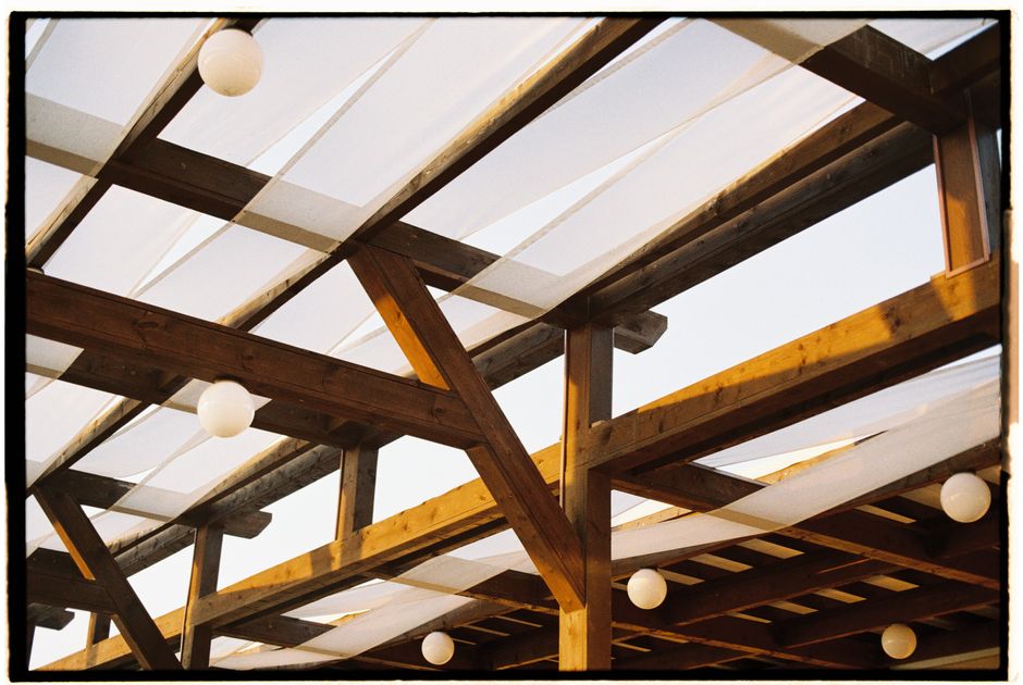 A detailed view of a rustic wooden pergola with white fabric and round light bulbs.
