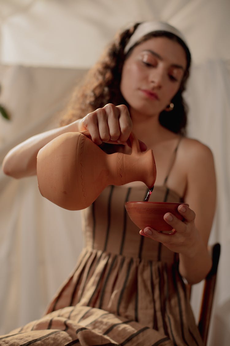 Woman Pouring Wine From Ceramic Jug Into Cup