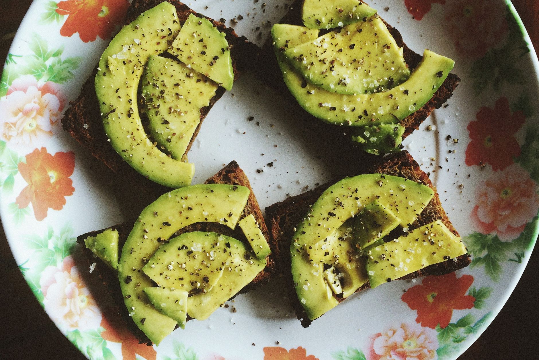 Sliced avocado on toast, garnished with spices on a floral plate, captured in natural lighting.