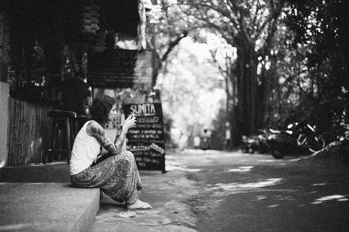 Free Black and white photo of a tattooed woman sitting on a street, using a smartphone. Stock Photo