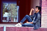 一个穿着牛仔布和皮夹克的时尚年轻人若有所思地坐在户外