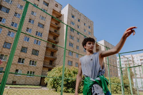 Man in Gray Sleeveless Shirt Standing near Green Fence