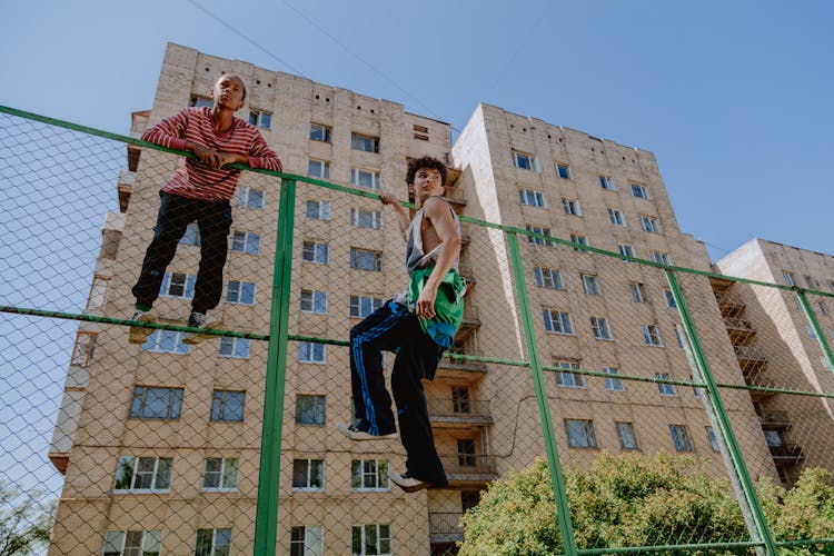 Boys Climbing The Metal Fence