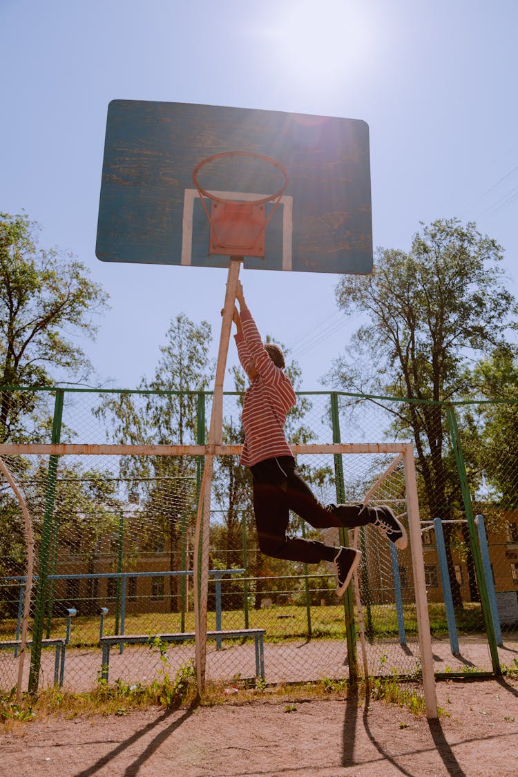 A Young Person Hanging From A Basketball Hoop