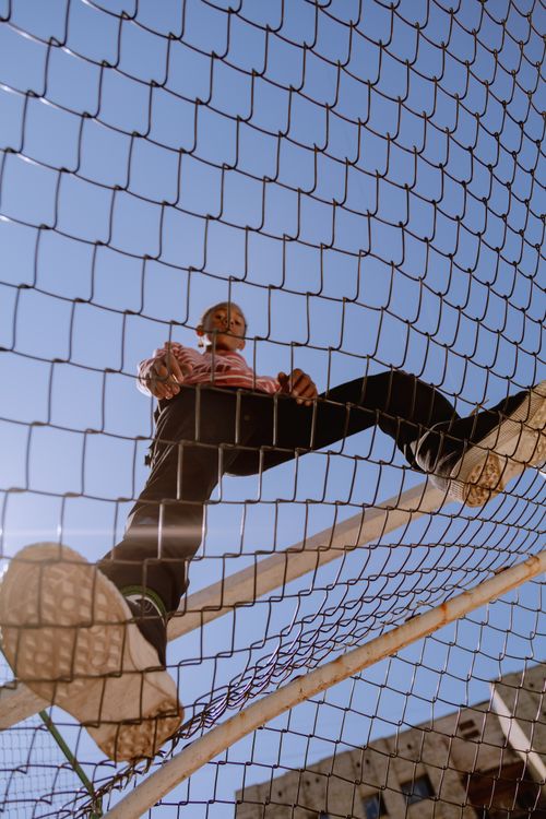 Free Low angle shot of a teenager standing on a fence against a clear blue sky. Stock Photo