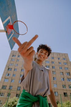 Teenage boy showing attitude under basketball hoop in sunny urban setting.