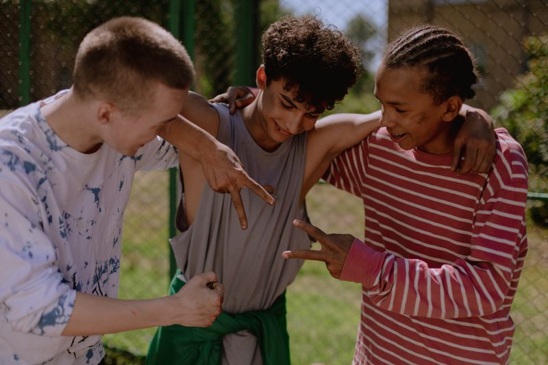 Three teenage friends play rock paper scissors outdoors, smiling and having fun.