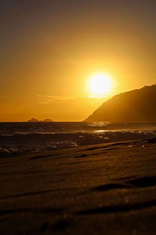 Free A stunning view of the sun setting over an ocean beach with gentle waves and silhouettes. Stock Photo