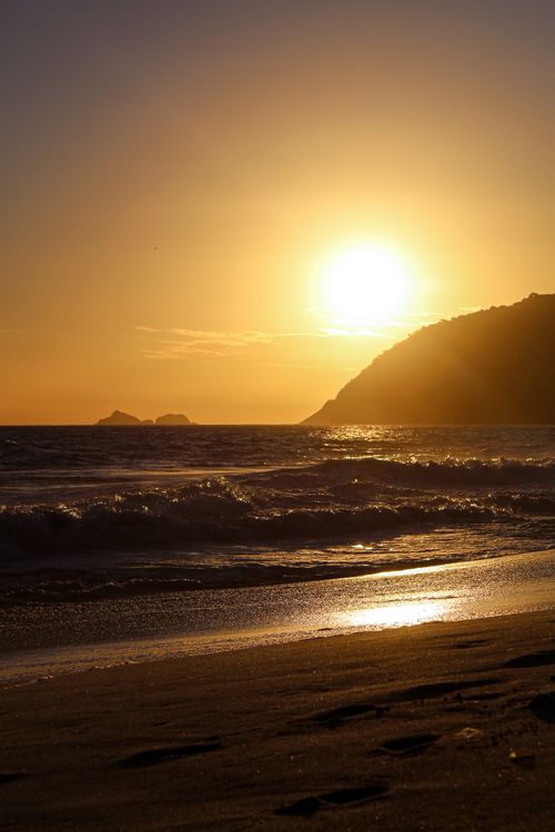 Free A tranquil sunset over the ocean, with waves gently reaching the sandy shore under warm golden hues. Stock Photo