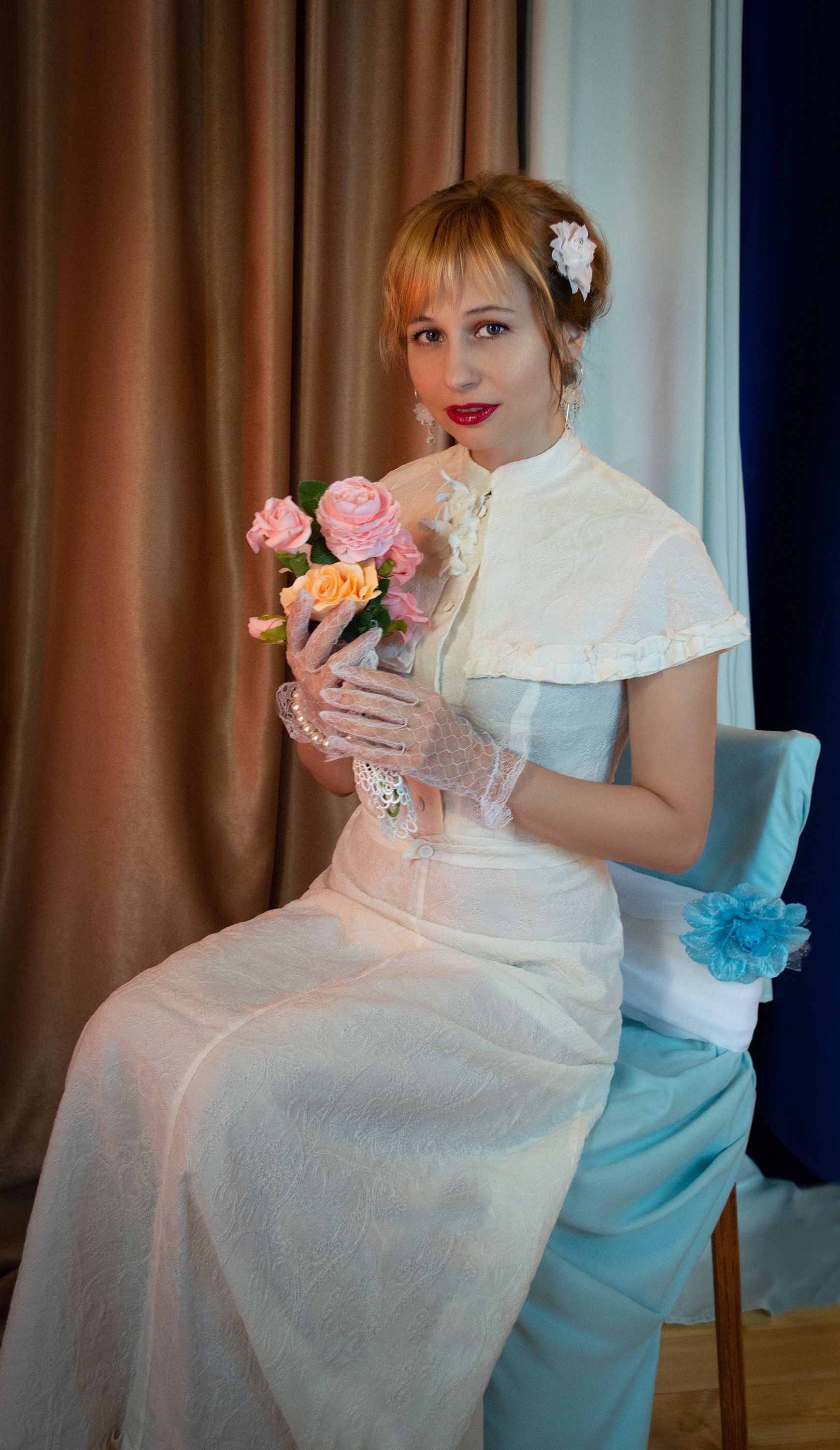 Elegant bride in white dress holding bouquet seated indoors, exuding classic charm.