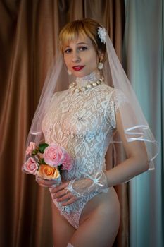 A beautiful bride poses in lace lingerie with a bouquet of roses, exuding elegance and charm.
