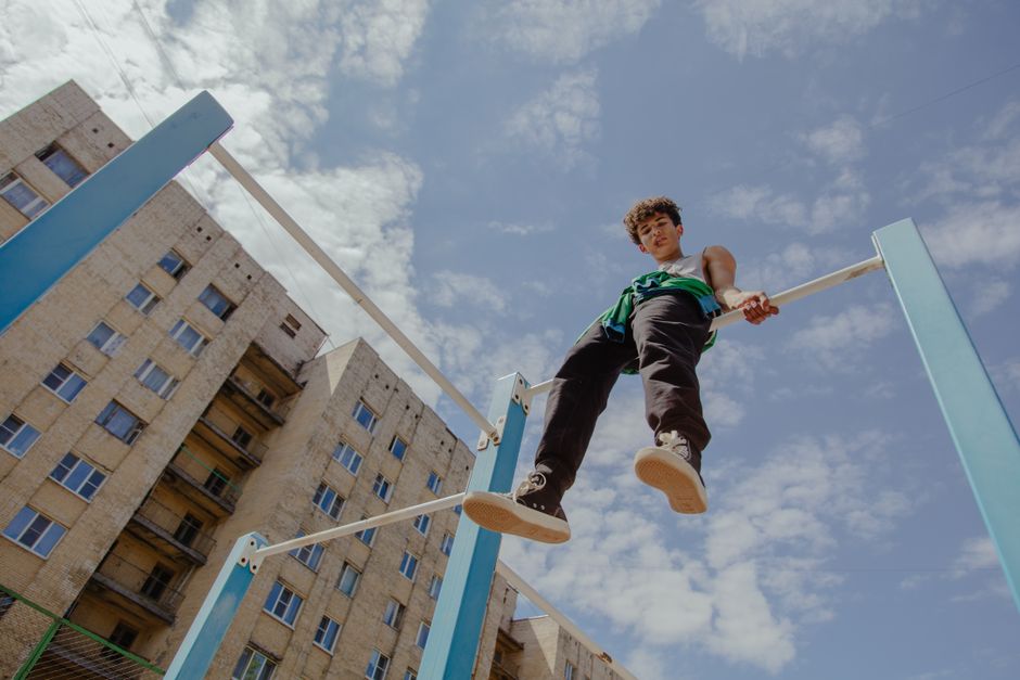 Teenager sitting on monkey bars in urban setting under clear blue sky.