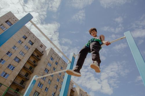 Free Teenager sitting on monkey bars in urban setting under clear blue sky. Stock Photo