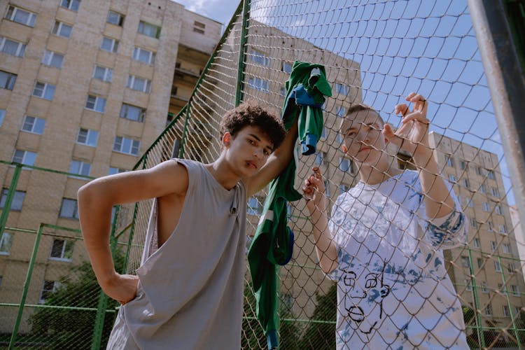 Two Young Boys Holding On Chain Link Fence