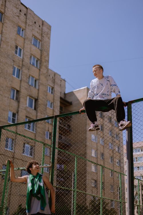 Free Two teenagers enjoy a sunny day at an urban basketball court, one sitting atop a fence. Stock Photo