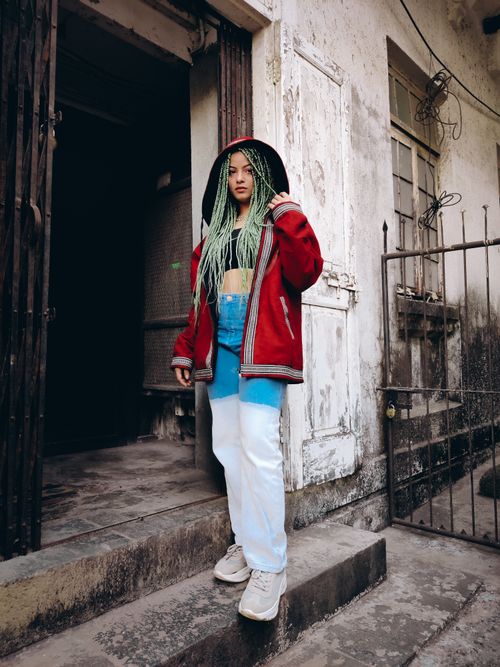 Free Woman with green box braids in casual attire standing by a rustic building entrance. Stock Photo