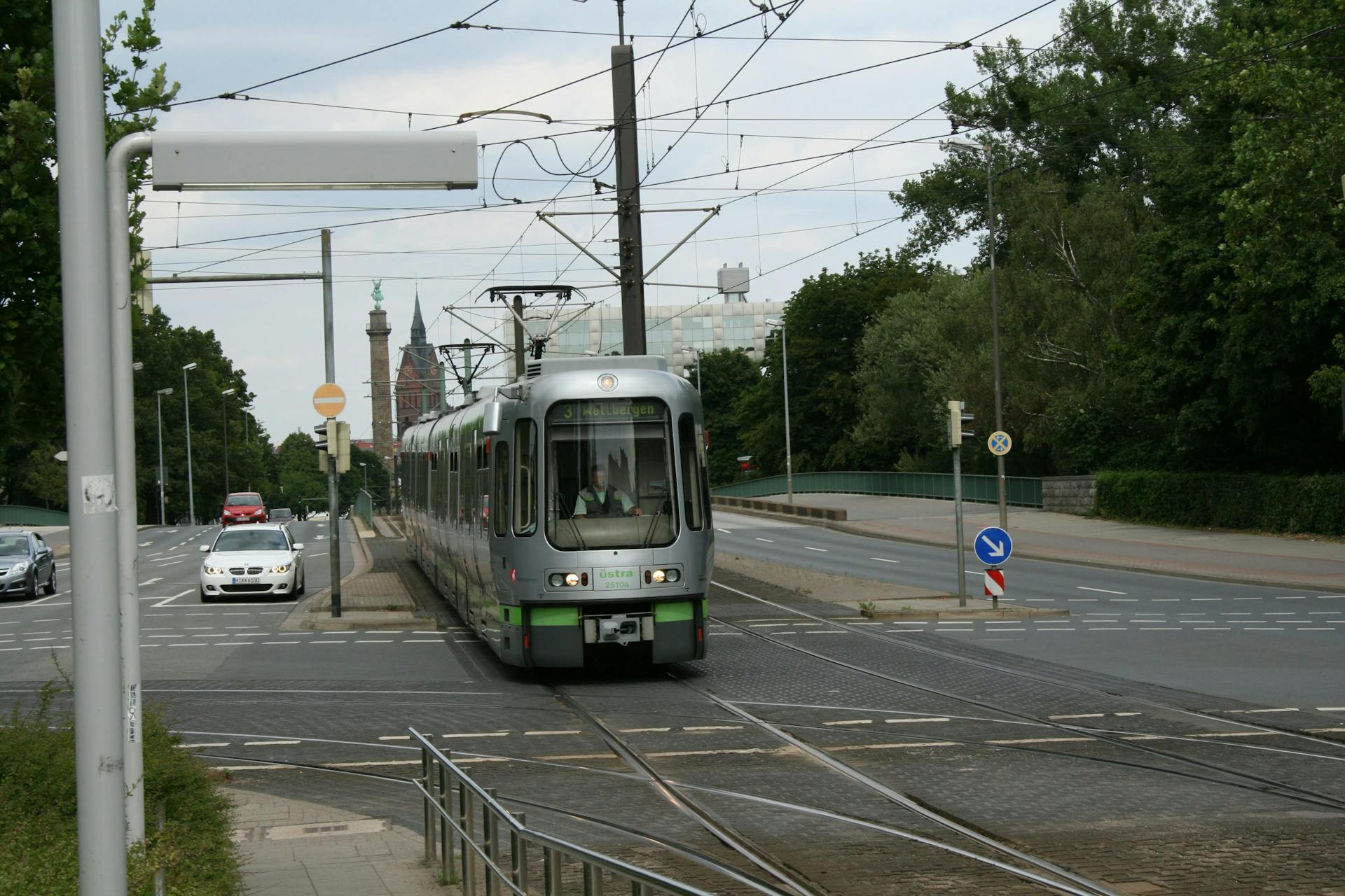 Silver tram moving through Hannover on a quiet street with trees and buildings in the background.