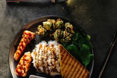 A gourmet dish featuring grilled salmon, rice, greens, and toast on a dark table setting.