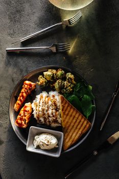 A gourmet dish featuring grilled salmon, rice, greens, and toast on a dark table setting.