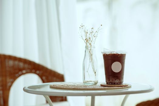 A stylish indoor scene with iced coffee and a glass vase on a woven mat.
