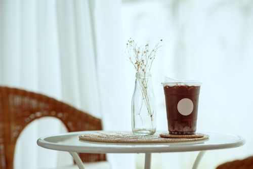 Free A stylish indoor scene with iced coffee and a glass vase on a woven mat. Stock Photo