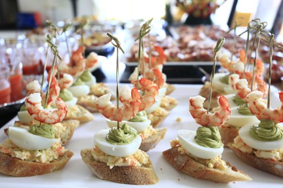 Rows of baguette pintxos with egg salad, egg slices, piped avocado cream and skewered shrimp