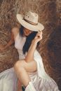 Woman in White Tank Top and White Skirt Wearing Brown Hat Sitting on Brown Grass