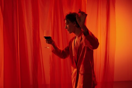 Man in a vibrant red suit dancing with a glass of wine in a dramatic studio setting.