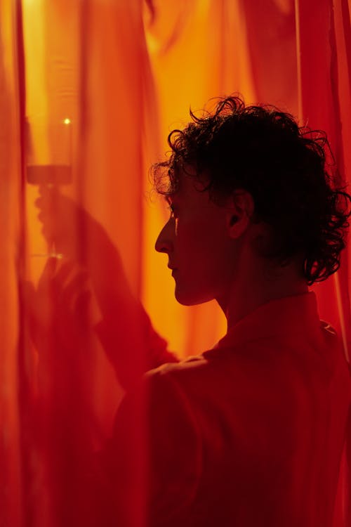 A Woman with Curly Hair Holding a Glass of Wine Behind a Sheer Curtain